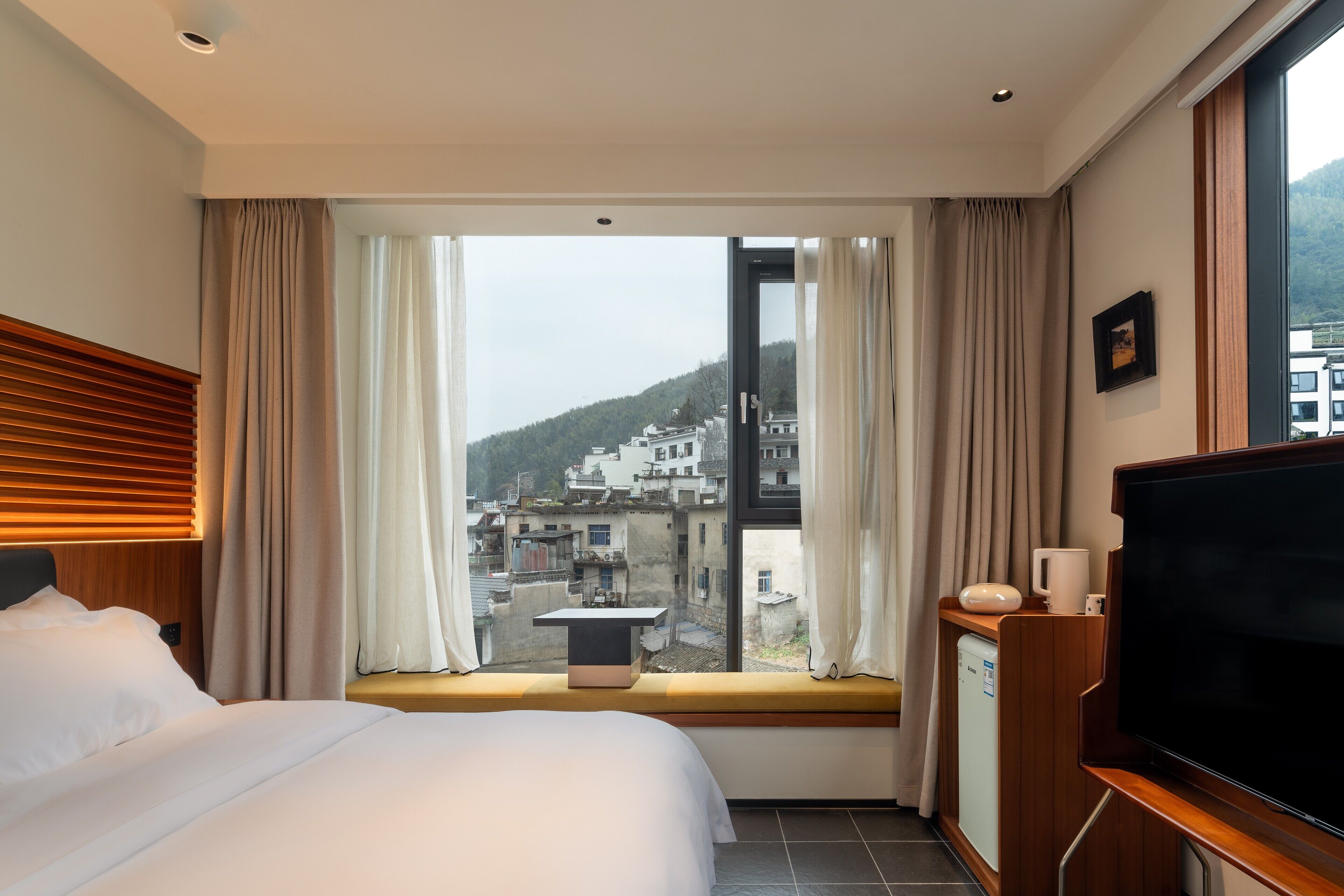 Een hotelkamer met een bed, een tafeltje, een televisie en een raam met gordijnen.