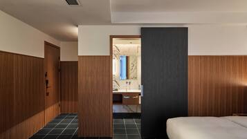 A modern hotel room with a wooden wardrobe, a marble-tiled bathroom, and a bed with a dark headboard.