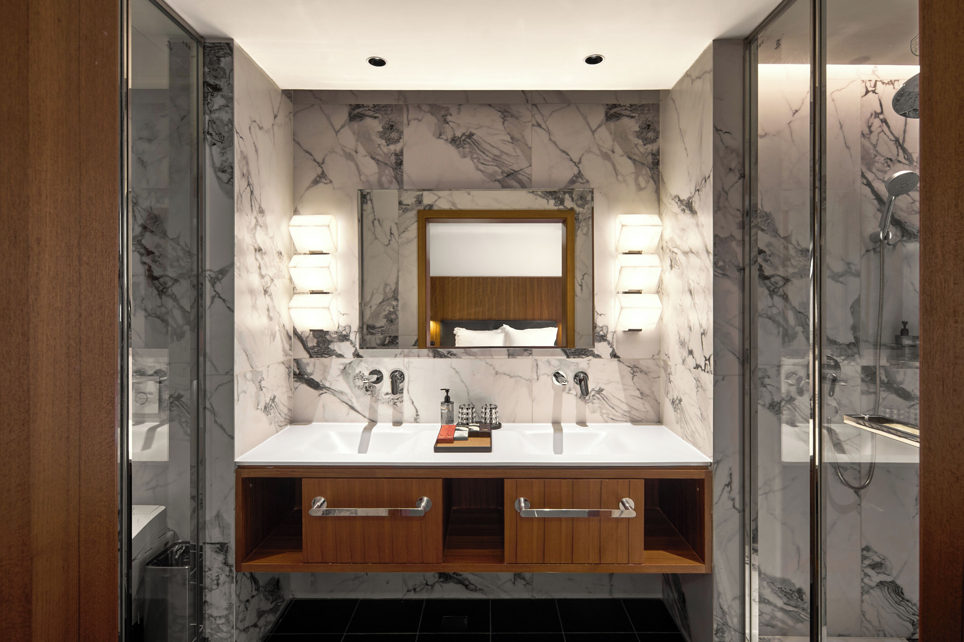 Une salle de bain moderne avec un pare-feu en marbre, deux vasques et un meuble-lavabo en bois doté de tiroirs.