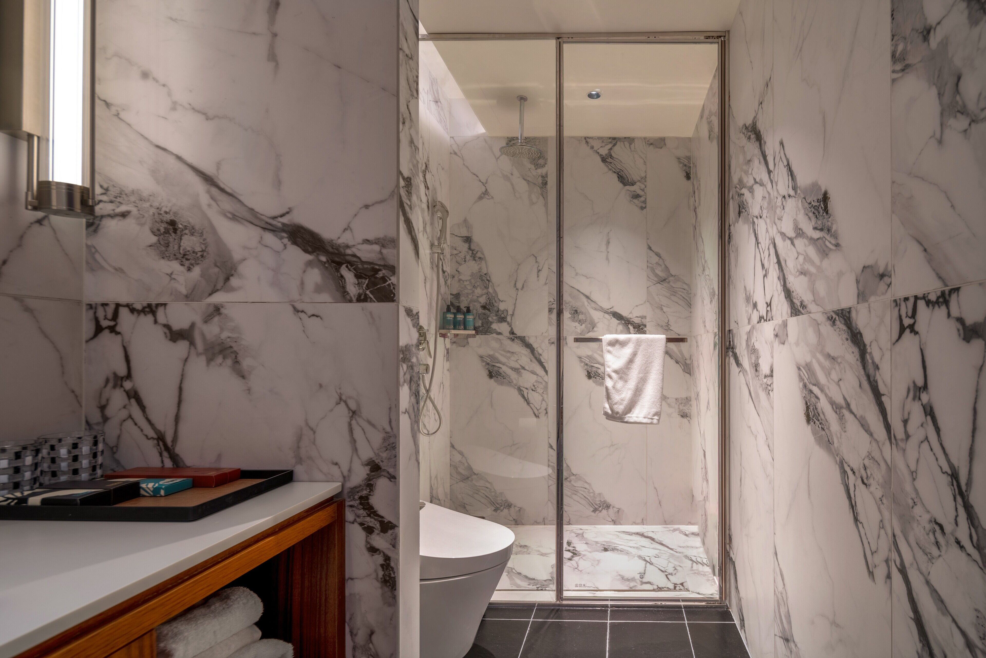 Une salle de bain moderne avec un mur décoré de motifs en marbre, une cabine de douche en verre et un lavabo blanc.