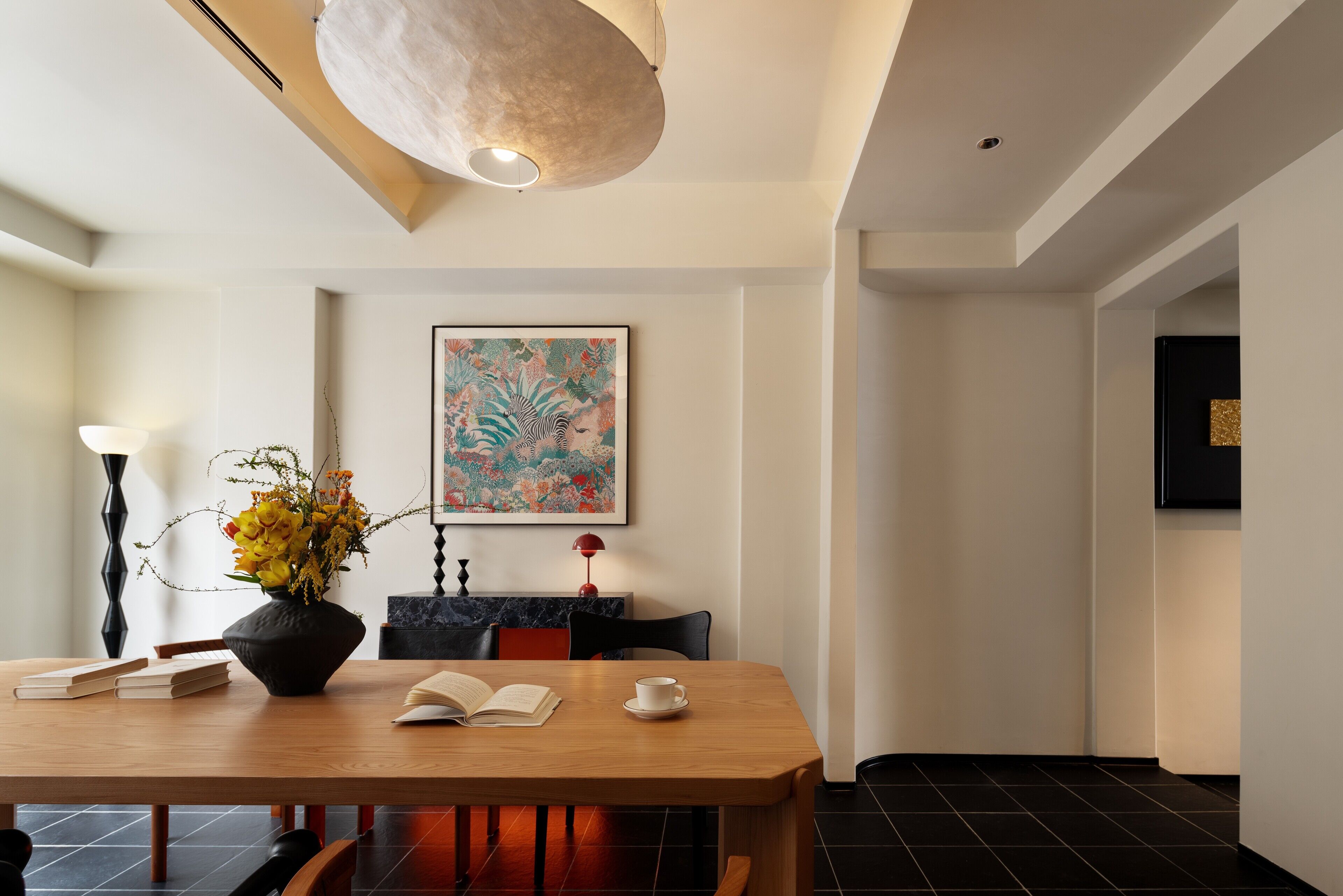 A dining area with a wooden table, books, a vase with flowers, and a painting on the wall.
