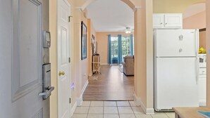 A hallway leading to a living room with a large window, a ceiling fan, and a refrigerator. - Barefoot IronWood 1613 Free Shuttle to Pool/Beach (North Myrtle Beach)