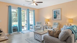 A spacious living room with a ceiling fan, two armchairs, a coffee table, and a painting on the wall. - Barefoot IronWood 1613 Free Shuttle to Pool/Beach (North Myrtle Beach)