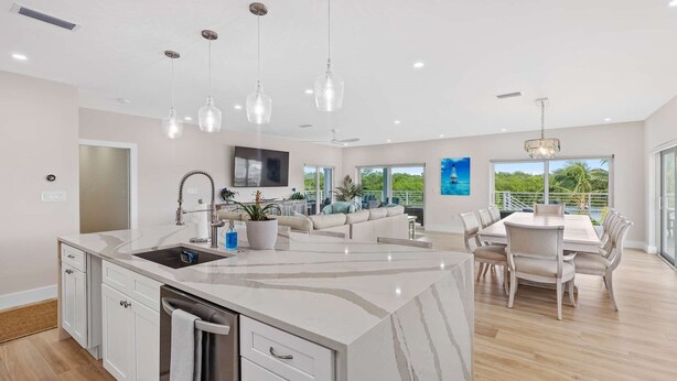 A modern kitchen with a marble island, a dining area with a round table, and a living space with a sofa and TV. - Sunset Point | Luxury 5 bdrm w pool, jacuzzi and XL dock, walk to beach (Marathon)