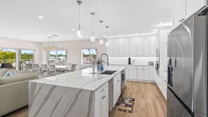 A modern kitchen with white cabinets, a marble island, stainless steel appliances, and pendant lighting. - Sunset Point | Luxury 5 bdrm w pool, jacuzzi and XL dock, walk to beach (Marathon)