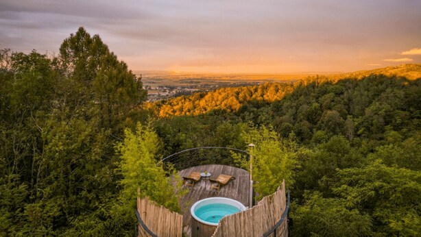 A wooden deck with a hot tub surrounded by dense forest, overlooking a valley.