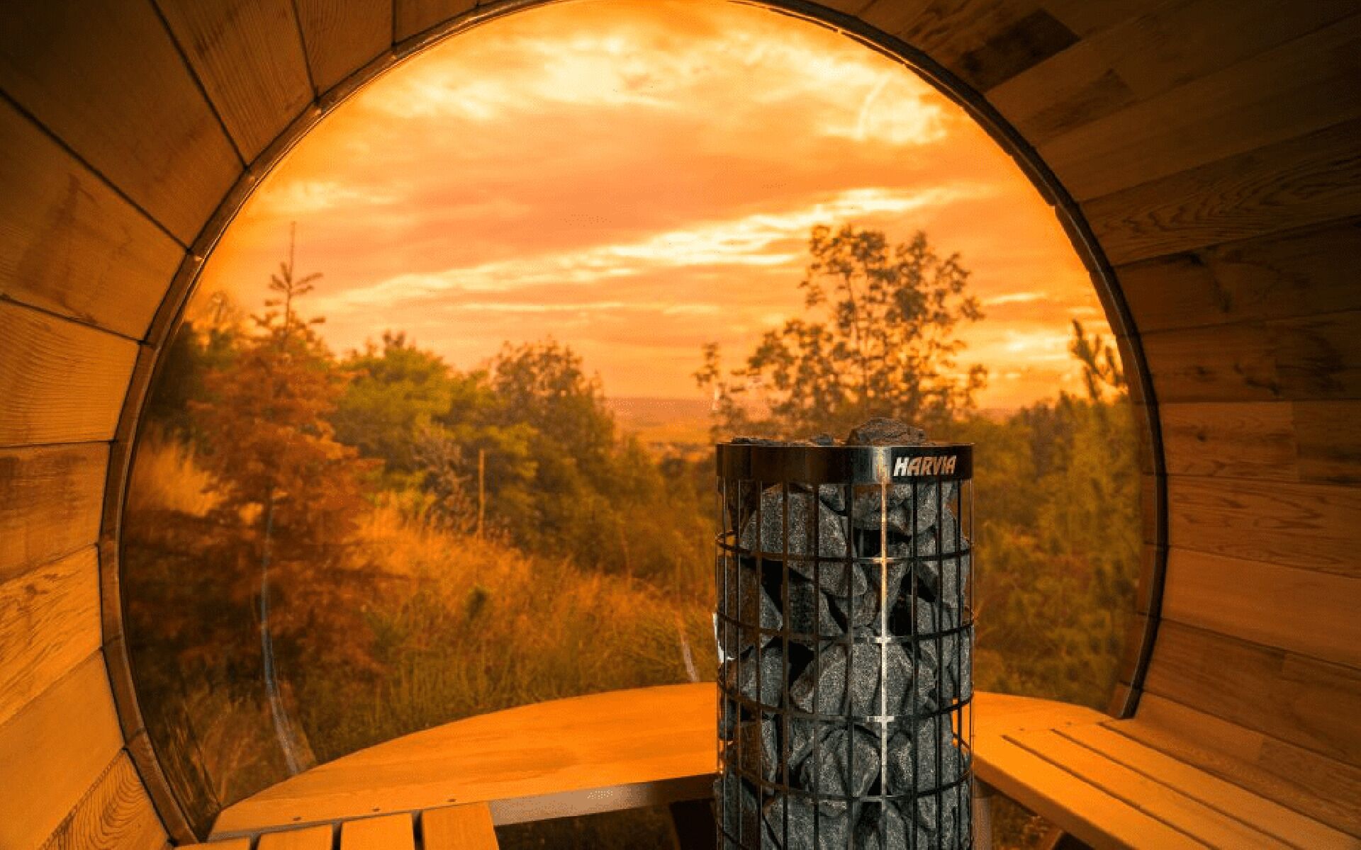 A circular window with a view of a sunset and a Harvia fireplace.