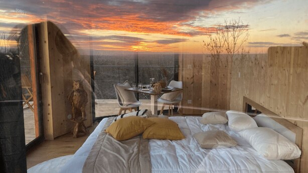 Une chambre à coucher avec un lit, des oreillers, une table avec des chaises et une vue sur le coucher de soleil.