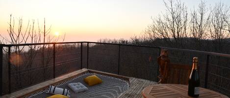 A wooden deck with a bench and cushions, a bottle of wine, and a statue of an owl.