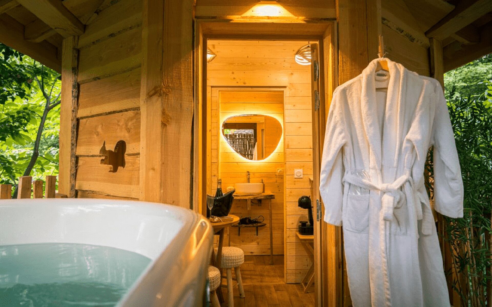 Een houten hutje van binnen, met een hottub, een badjas en een spiegel met een hartvormig lijstwerk.