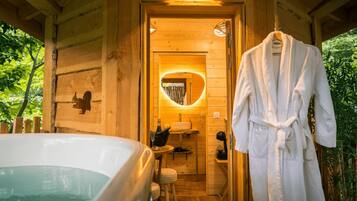 Een houten hutje van binnen, met een hottub, een badjas en een spiegel met een hartvormig lijstwerk.