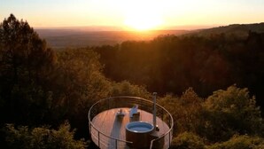 Eine runde Aussichtsplattform mit Whirlpool, umgeben von bewaldeten Hügeln, während der Sonnenuntergang.