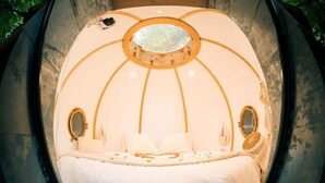 A circular room with a bed centered, two side mirrors, and a circular window above the bed.