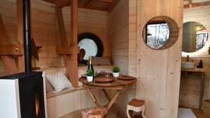 A wooden cabin interior with a dining table set, a fireplace, and a round mirror on the wall.