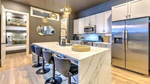 A modern kitchen with a large island, bar stools, stainless steel appliances, and a view of the outdoors. - Expansive 4BR/5BA DT Home with Hot Tub & Game Room (Nashville)
