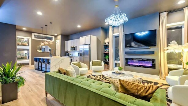 A modern living room with a green sofa, white armchairs, a dining area, and a kitchen. - Expansive 4BR/5BA DT Home with Hot Tub & Game Room (Nashville)