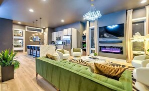 Ein modernes Wohnzimmer mit einem grünen Sofa, weißen Sesseln, einem Essbereich und einer Küche.