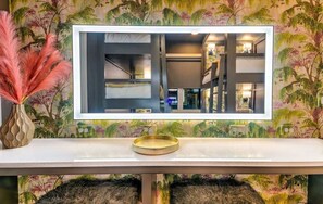 A modern bathroom with a large mirror, a white vanity, and a decorative vase.