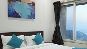 Ein ordentlich bezogenes Bett mit einer petrolfarbenen gesteppten Tagesdecke und zwei petrolfarbenen Kissen, ein großes abstraktes Gemälde an der Wand und ein Fenster mit Blick auf eine Landschaft.