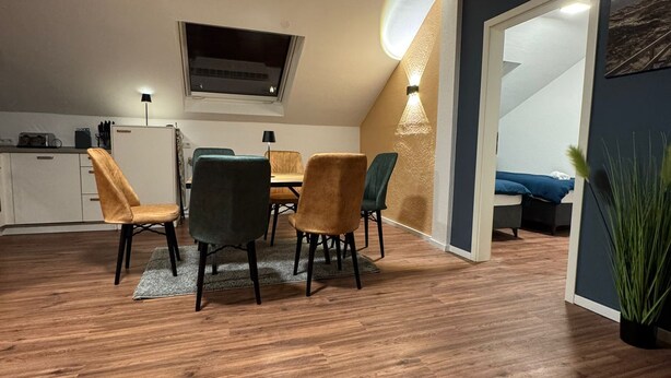 A dining area with a wooden floor, a table with chairs, a TV mounted on the wall, and a plant. - City Oasis - Central vacation apartment (Nürnberg)