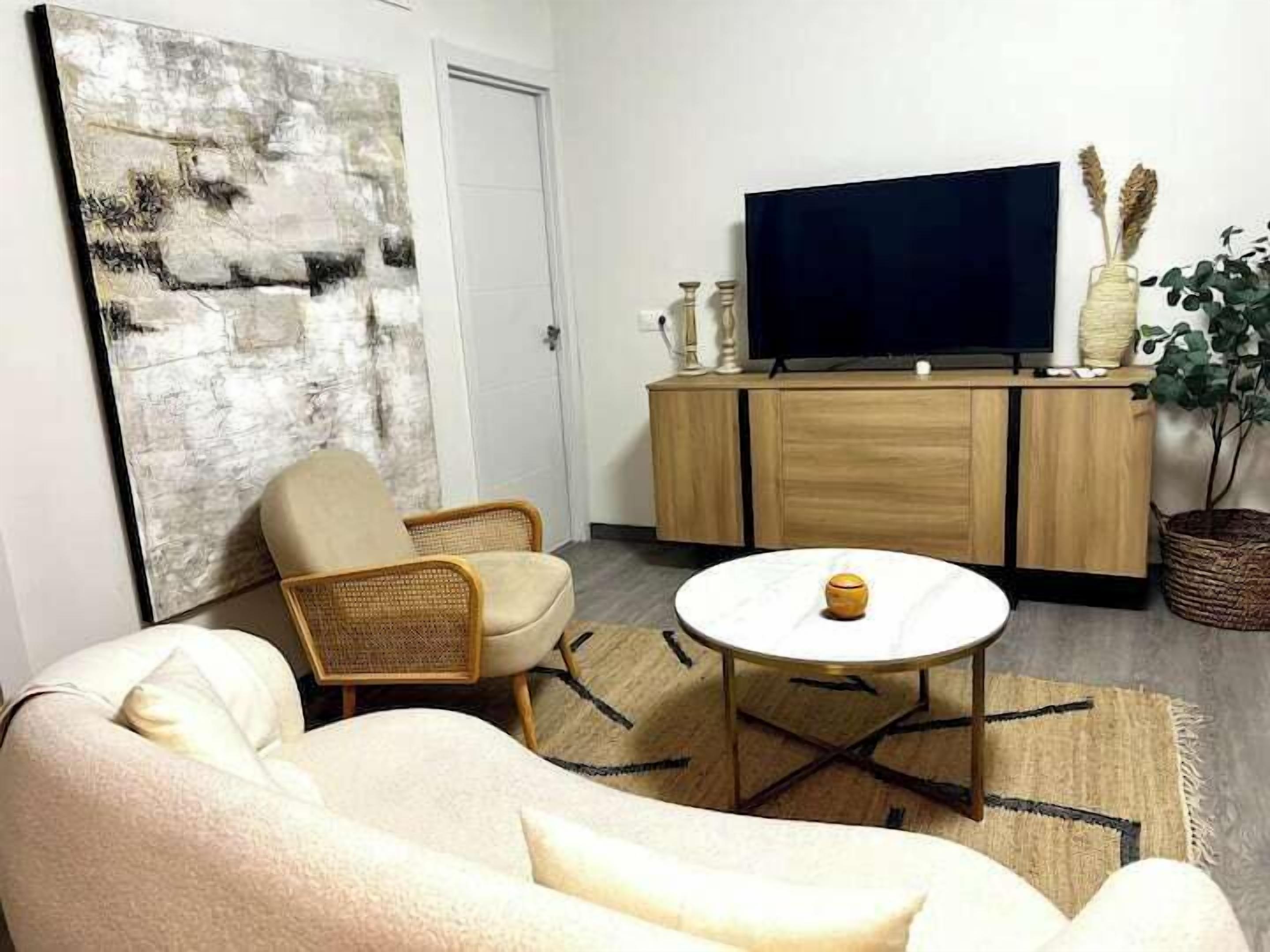 A living room with a sofa, a coffee table, a TV on a wooden cabinet, and a large abstract painting.