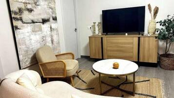 A living room with a sofa, a coffee table, a TV on a wooden cabinet, and a large abstract painting.