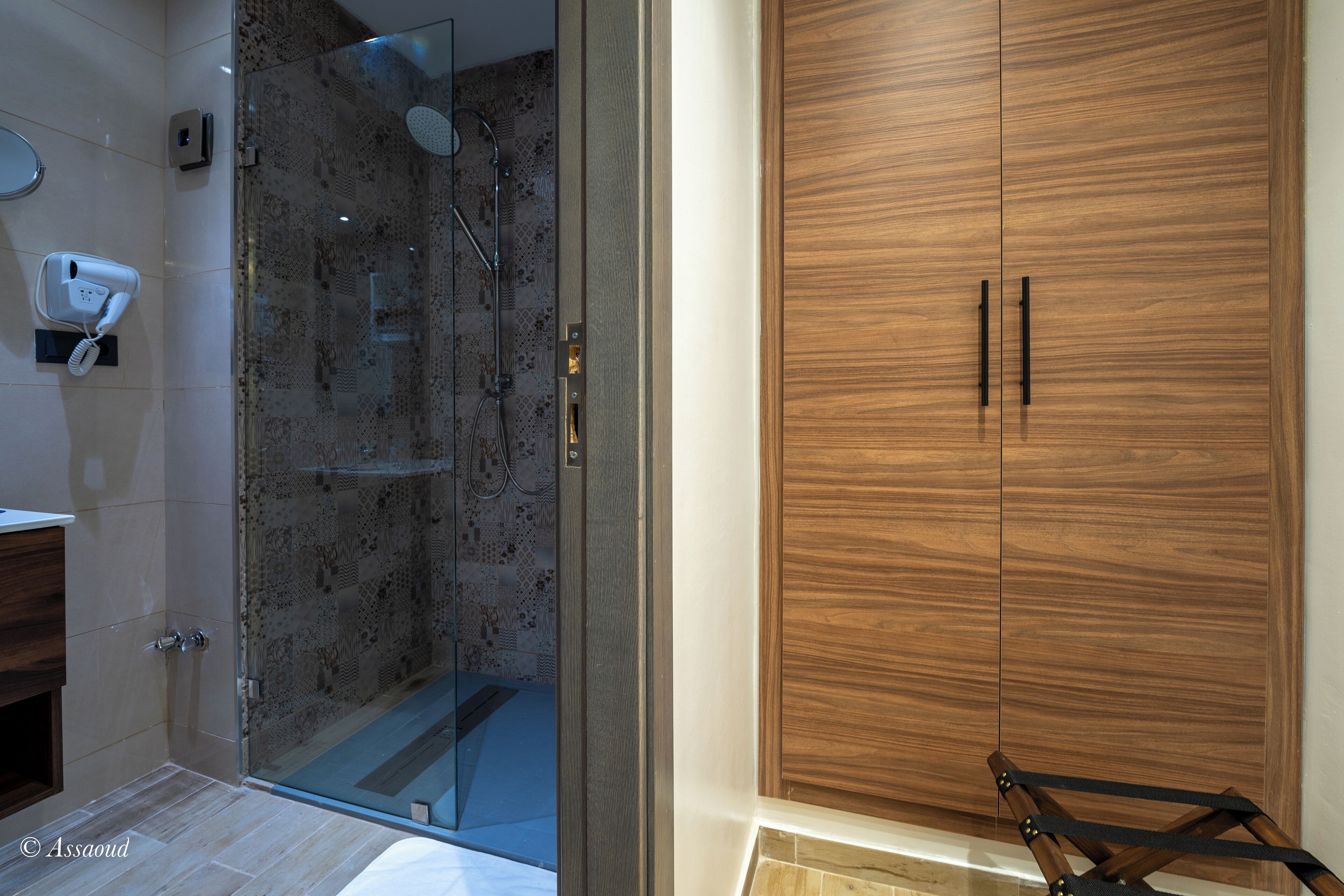 A modern bathroom with a glass-enclosed shower, a wooden wardrobe, and a hairdryer on the wall.