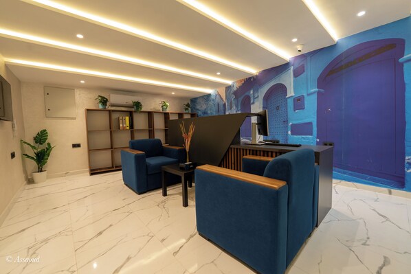 Un vestíbulo moderno con suelo de mármol, asientos azules, un mostrador de recepción y un mural en la pared.