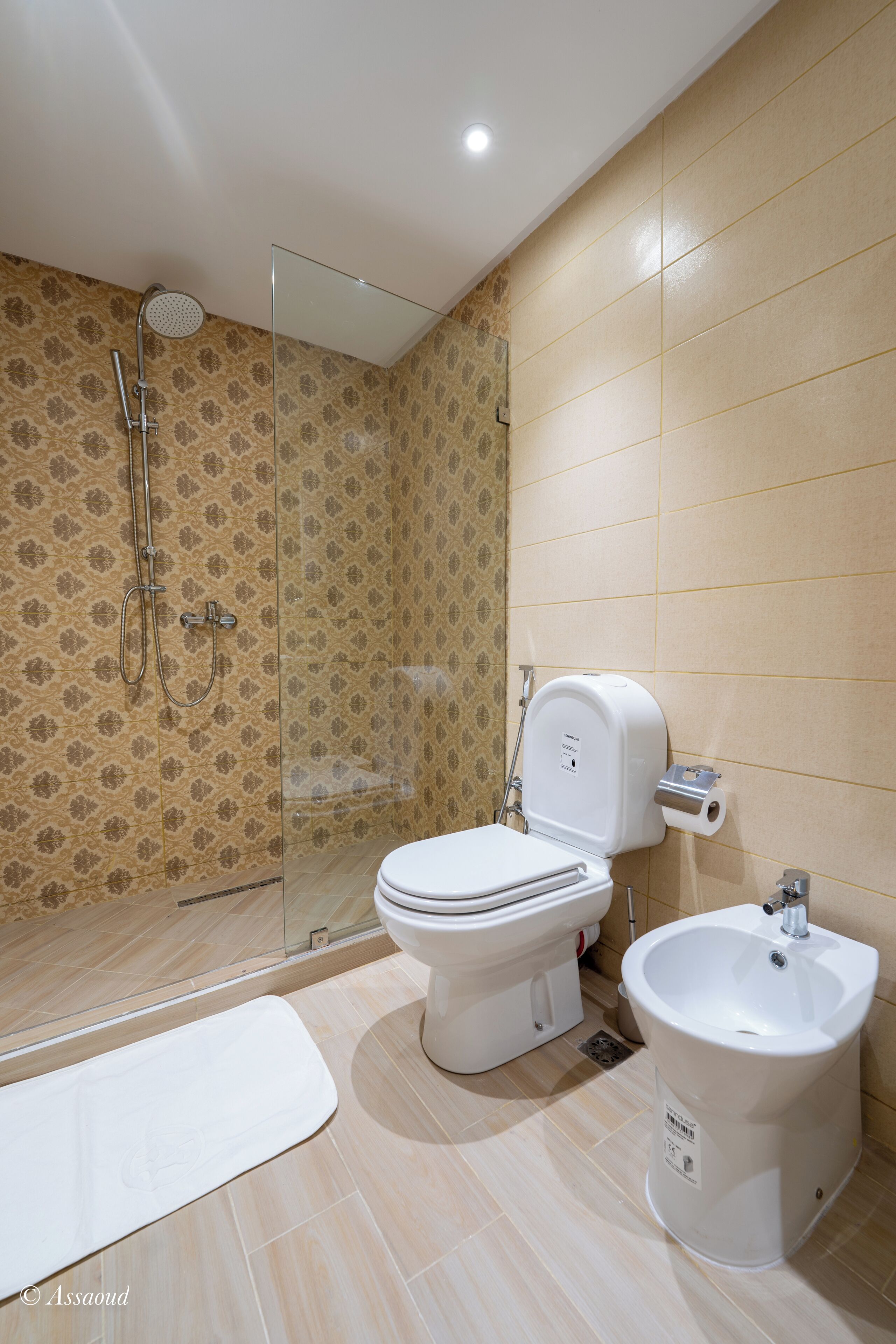 Un baño con ducha, inodoro, bidé y cabina de ducha con mampara de vidrio.