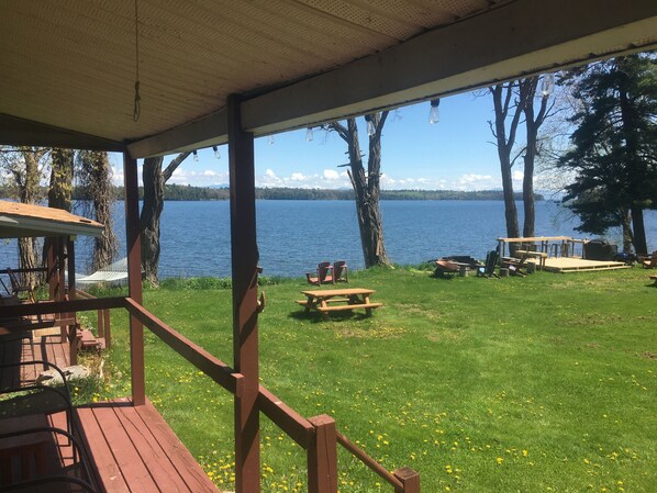 A covered deck with picnic tables and chairs overlooking a lake. - Lakeside Cottage #305 at Valcour Cottages (Plattsburgh)