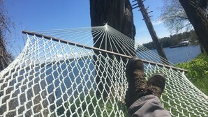 A hammock tied between trees with a view of a lake and a building in the background. - Lakeside Cottage #305 at Valcour Cottages (Plattsburgh)