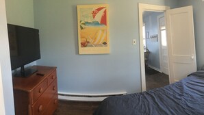 A bedroom with a bed, a dresser, a TV, and a door leading to another room. - Lakeside Cottage #305 at Valcour Cottages (Plattsburgh)