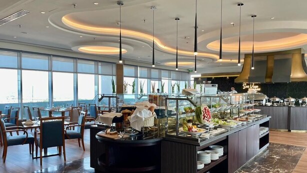A modern hotel lobby with a buffet area, seating arrangements, and large windows offering a view.