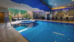 A swimming pool with a tiled floor, a seating area with chairs and a table, and a wall with a nature-themed mural.