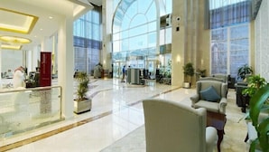 A spacious lobby with a high ceiling, large windows, and a central seating area with armchairs.
