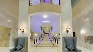 Um hall imponente com uma escadaria central, piso de mármore e duas poltronas de cada lado.