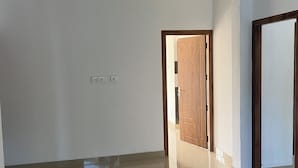Un'ampia stanza vuota con pavimento piastrellato lucido, pareti bianche e una porta in legno.