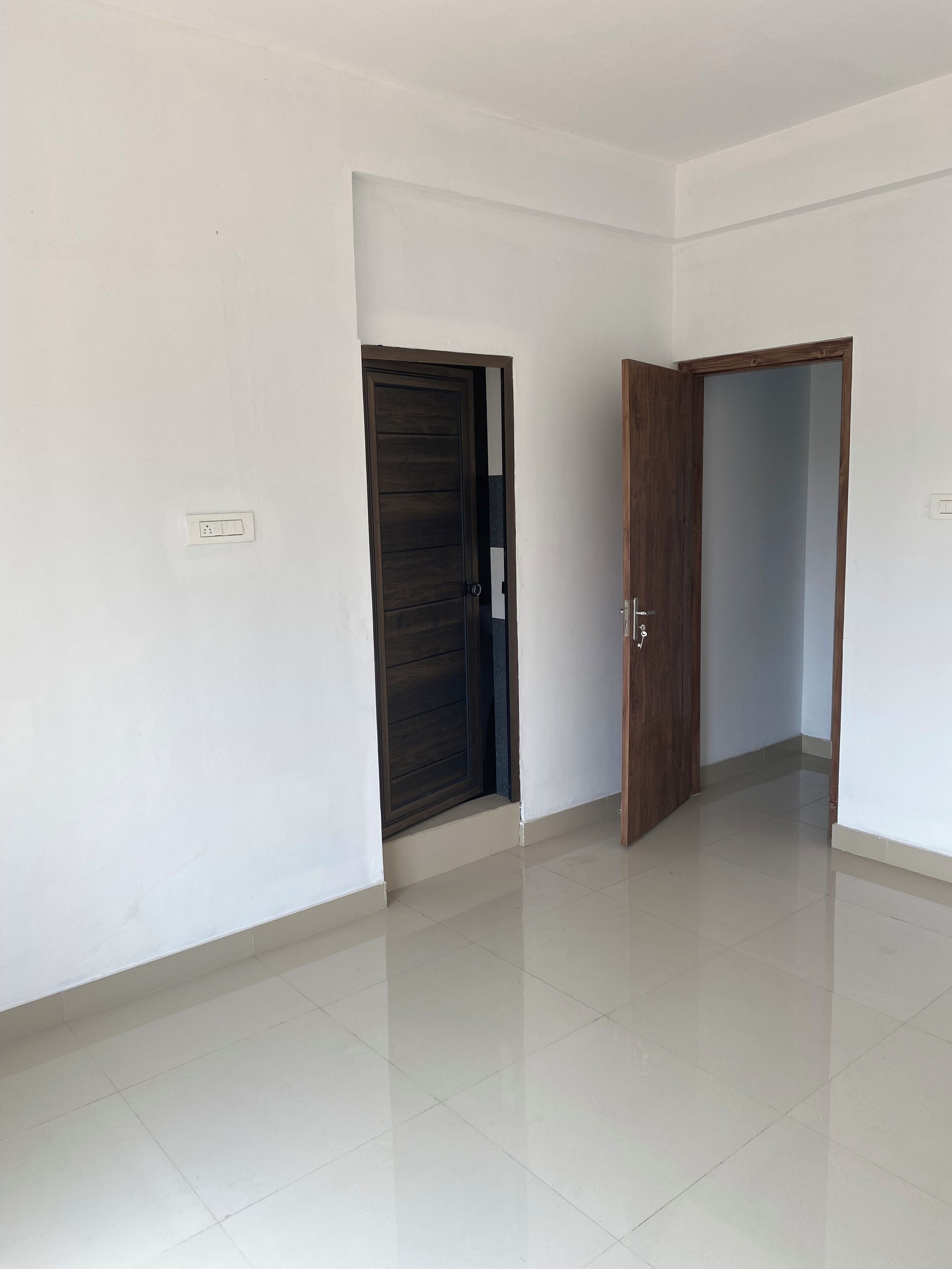 Una habitación con paredes blancas, suelo de baldosas y dos puertas de madera.