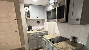 A modern kitchen with grey cabinets, a stainless steel microwave, and a granite countertop.