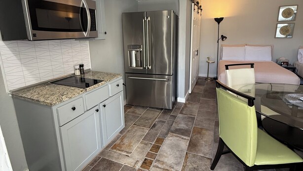 A modern kitchen with stainless steel appliances, a granite countertop, and a dining area with a glass table and a green chair.