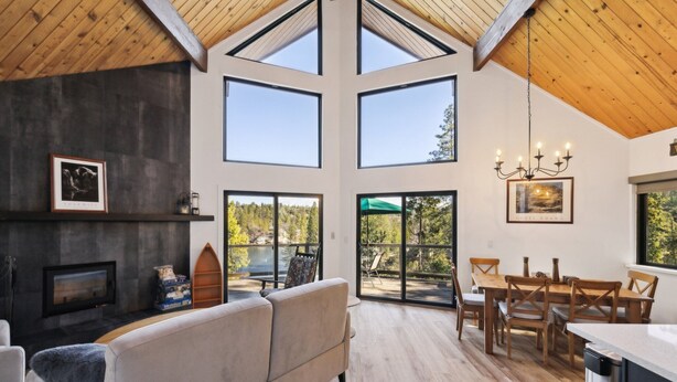 Amplia sala de estar con chimenea, un sofá grande y una mesa de comedor con sillas. Grandes ventanales que ofrecen luz natural y vistas al exterior.