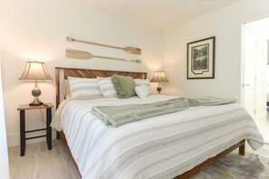 A neatly made bed with a striped bedspread, two bedside tables with lamps, a wooden headboard, and a framed picture on the wall. - The White House On Flagler Beach - Unit 22 2 Bedroom Home (Flagler Beach)