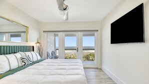 A bedroom with a large bed, a TV mounted on the wall, and a sliding glass door leading to a balcony.
