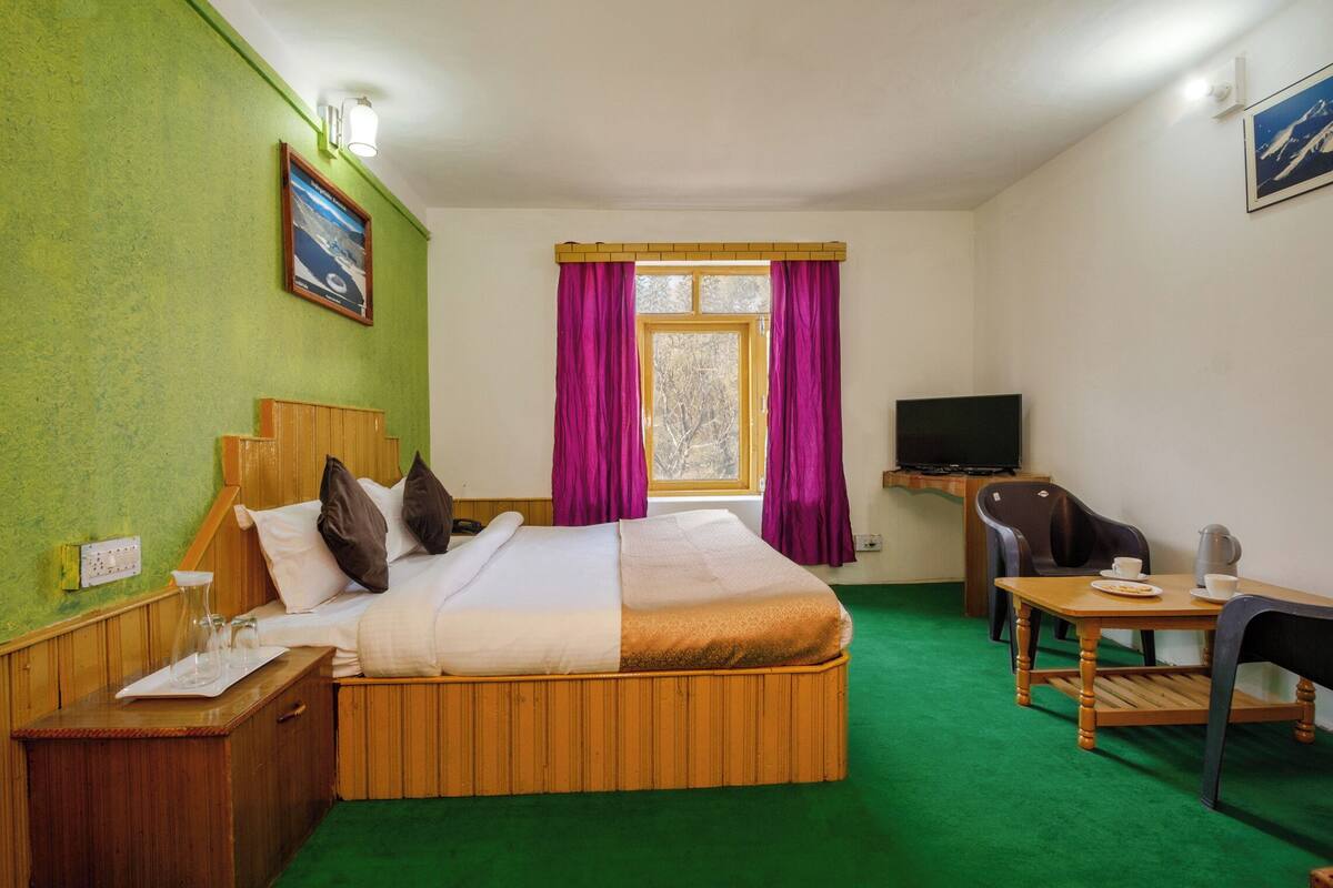 A hotel room with a bed, a desk with a chair, a television, and a window with curtains.