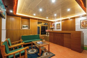 A reception area with wooden paneling, a green sofa, wooden chairs, a glass coffee table, and a reception desk.