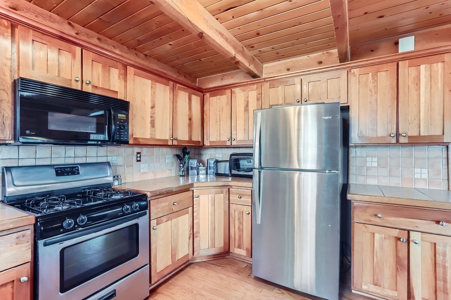 A kitchen with wooden cabinets, a stainless steel refrigerator, a microwave, and a stove.