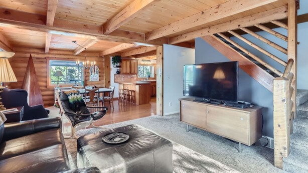A spacious log cabin interior with a dining area, a living room with a leather sofa, a TV, and a staircase. - Valley View Vistas 3 Bedroom Lodge (Nederland)