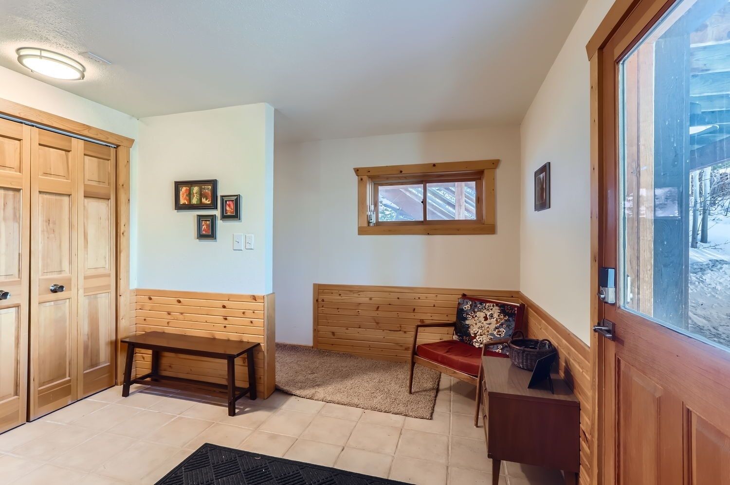 A room with wooden walls and a window, a bench, a table, and a door.