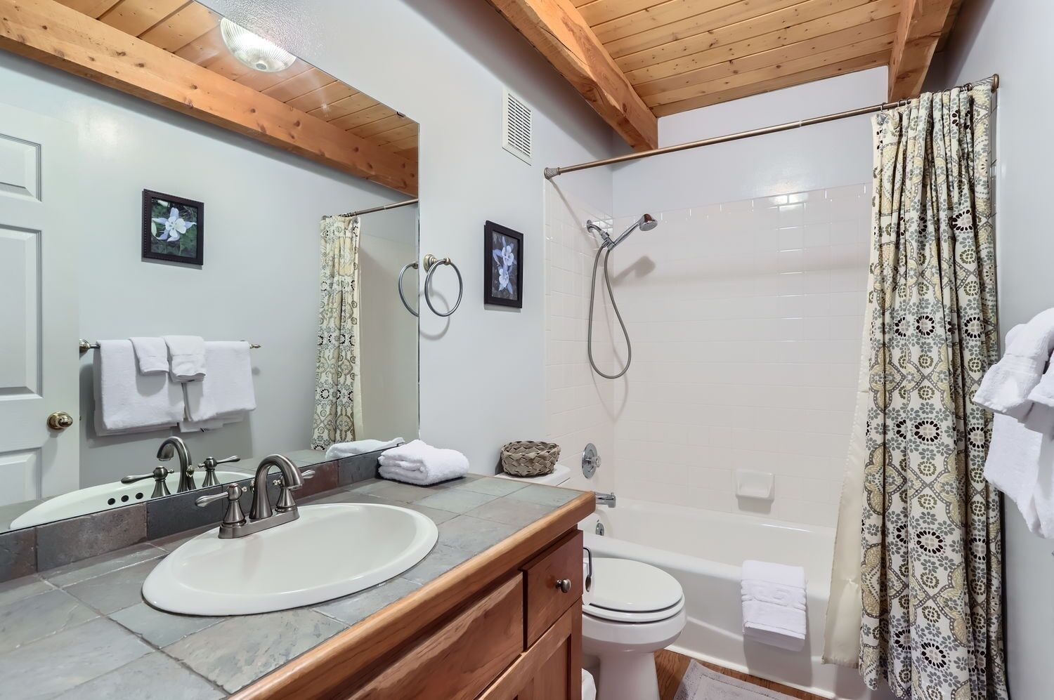 Une salle de bain équipée d’un lavabo, d’un miroir, de toilettes, d’une douche et de poutres en bois au plafond.
