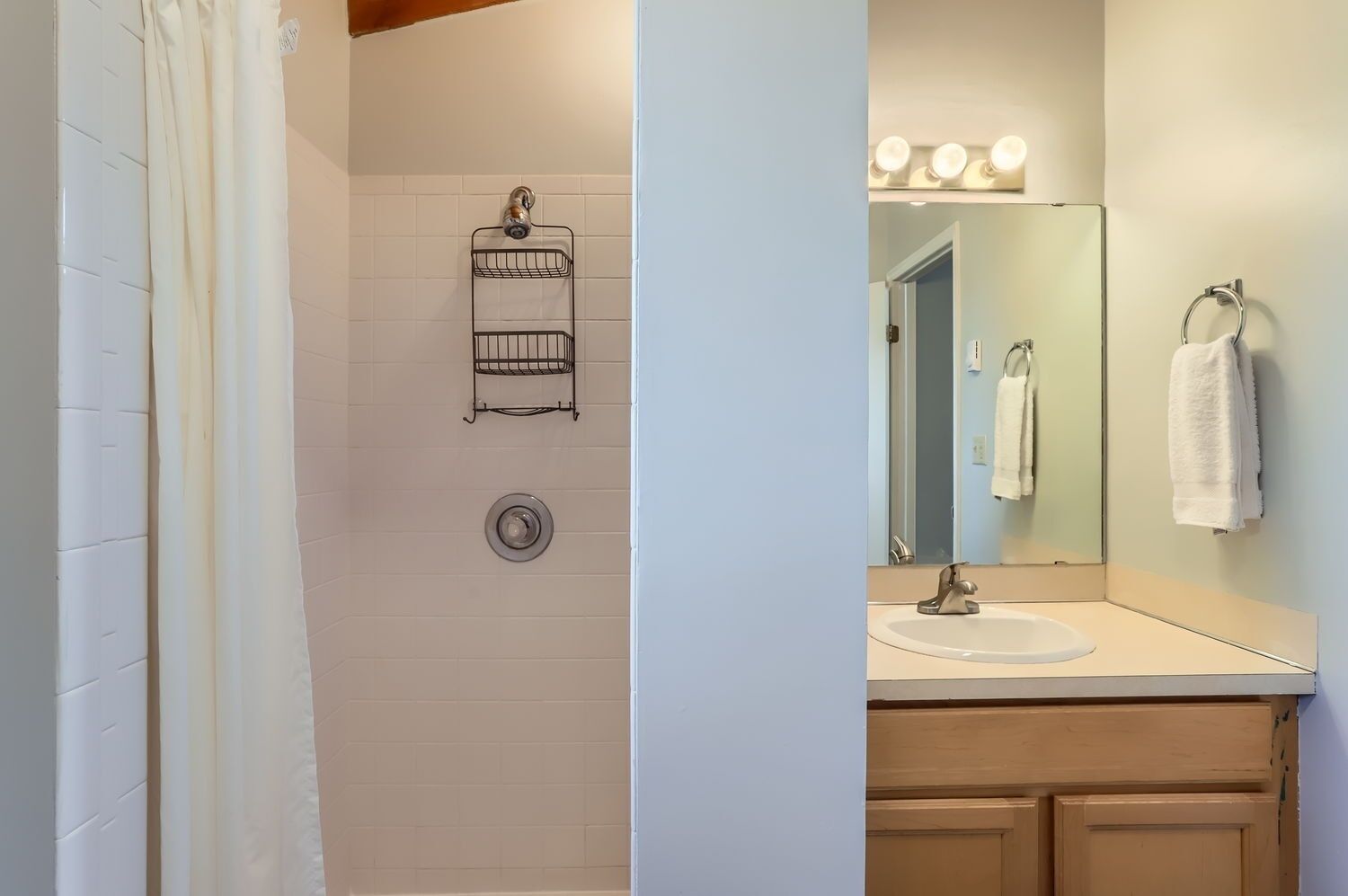 Een badkamer met een douche, wastafel, spiegel en handdoekrek.
